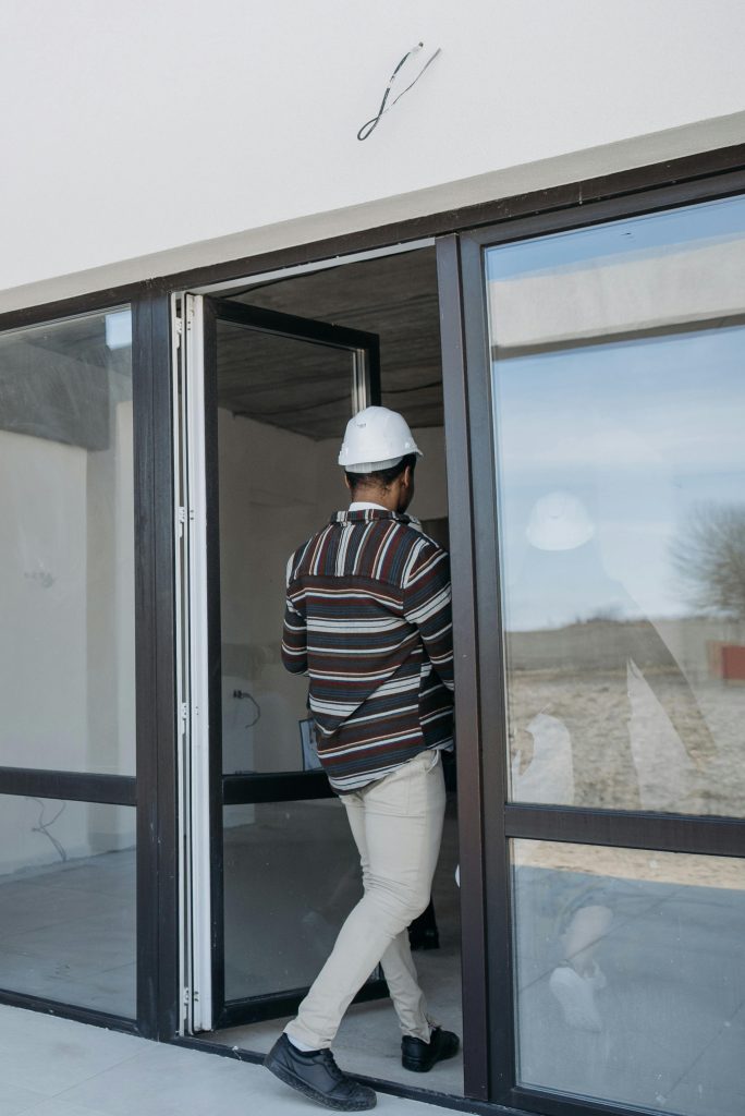 A real estate agent inspects a new property entrance wearing a white helmet by a glass door.