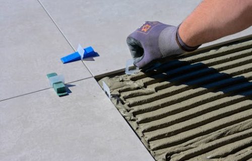 Detailed view of gloved hand aligning tiles with levelers and spacers during construction.